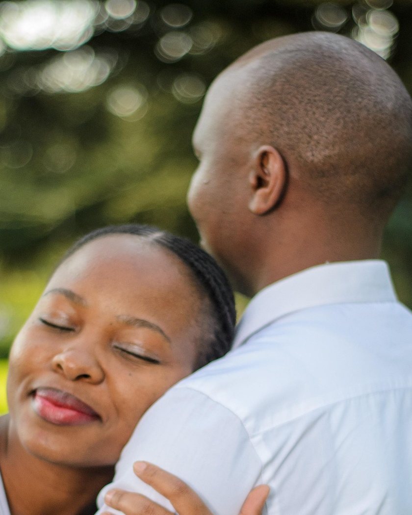 A woman resting her head on her partner's shoulder, eyes closed and smiling