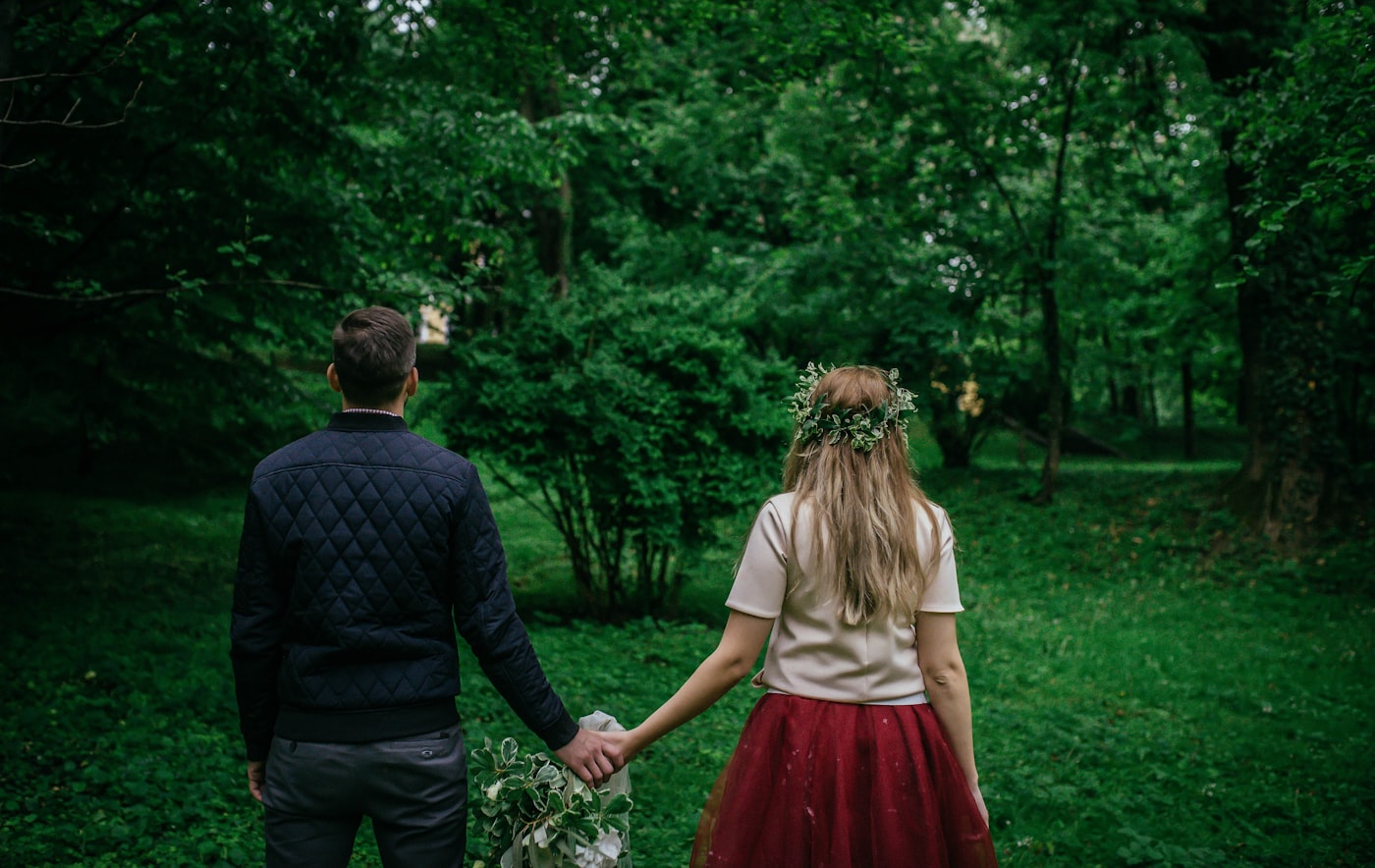 A couple holding hands, walking into a lush green forest together