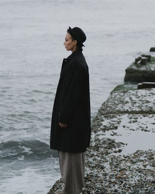A woman standing alone on a grey pier, looking out to sea