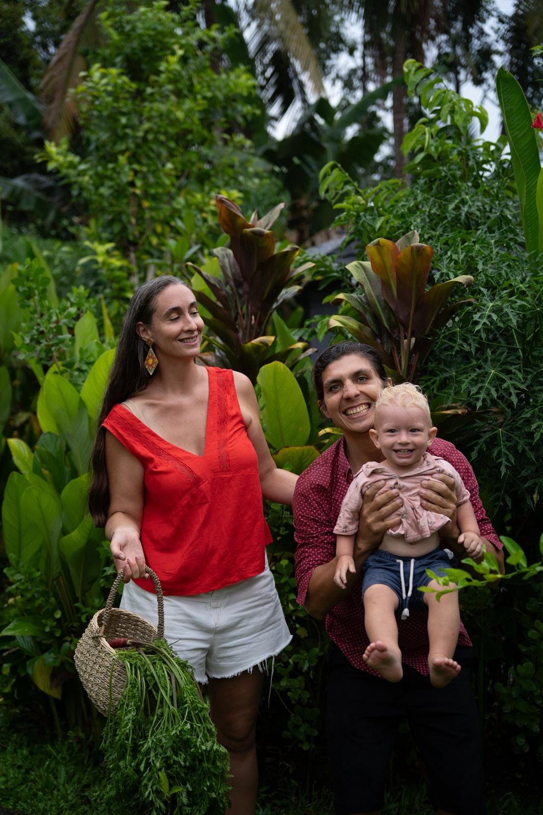 Adam and Andréanne smiling together with their son in their lush garden in Bali