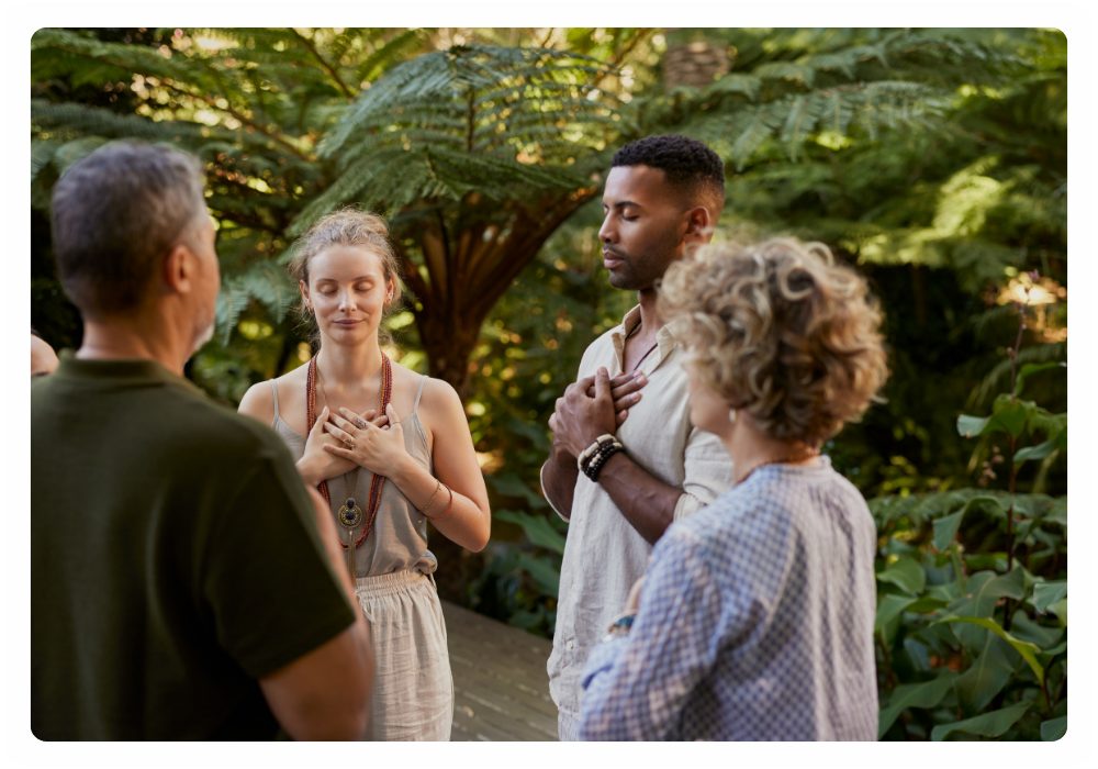 A circle of people standing in a lush garden with their hands resting on their hearts