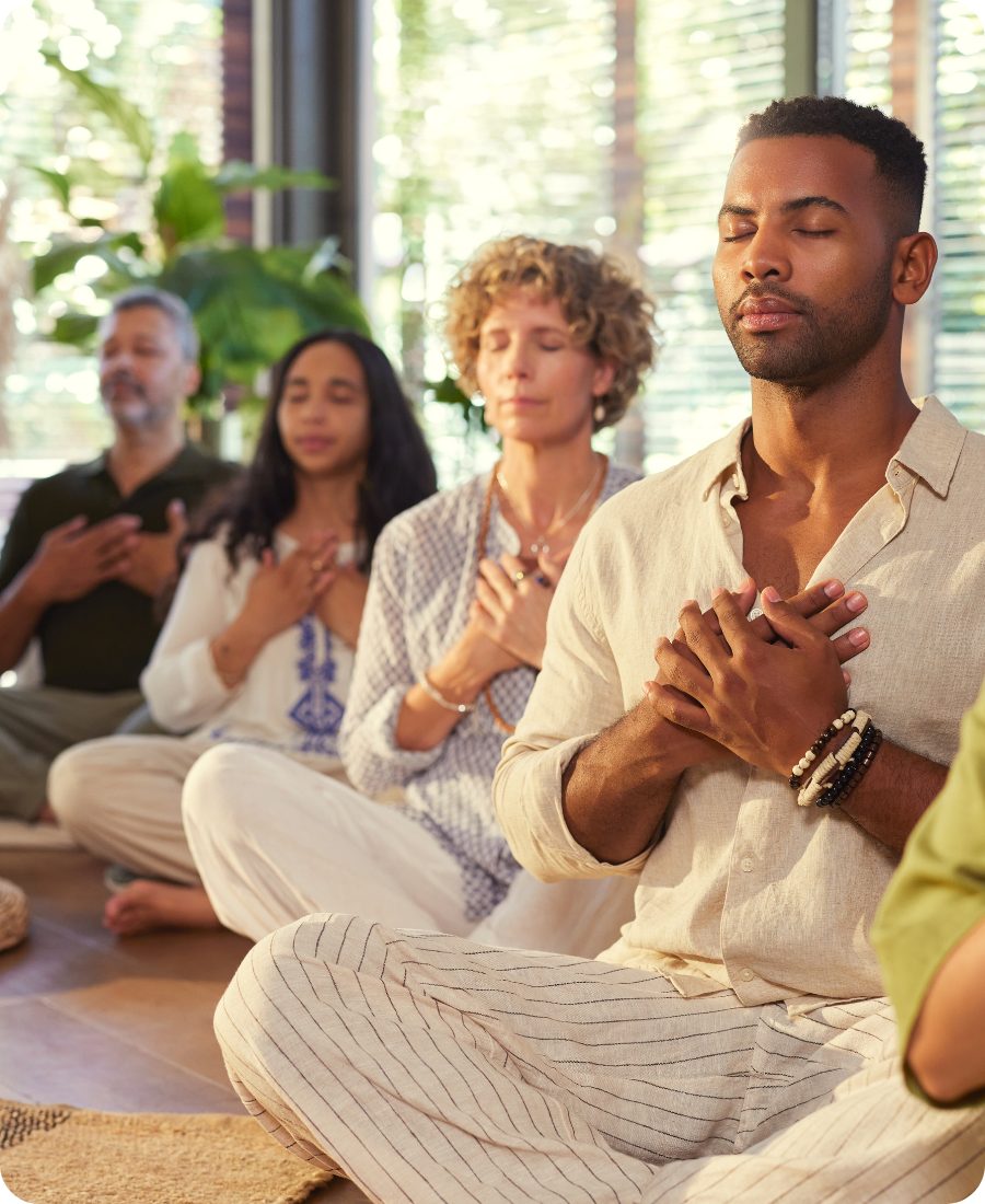 A circle of people meditating together with their hands on their hearts, calm and at ease