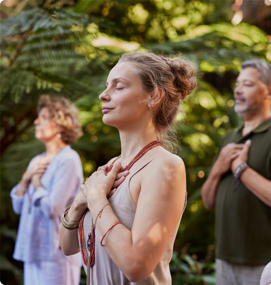 A woman standing in a lush garden with her hands resting on her heart, eyes closed