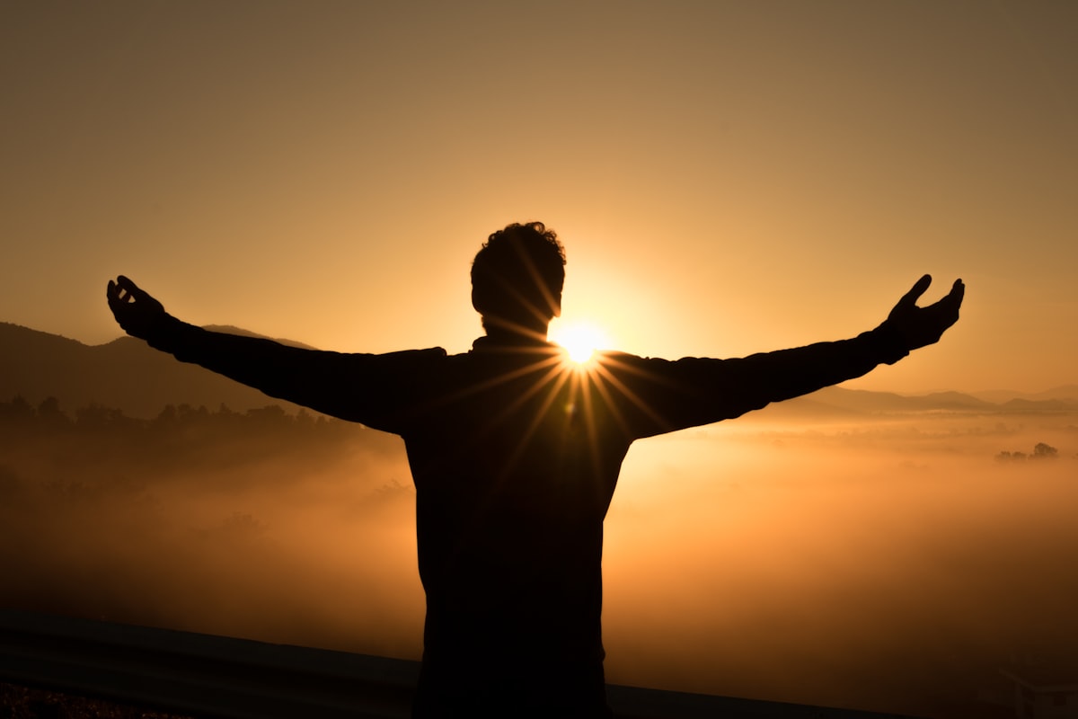 A man greeting the sunrise with open arms — peace, freedom, and love